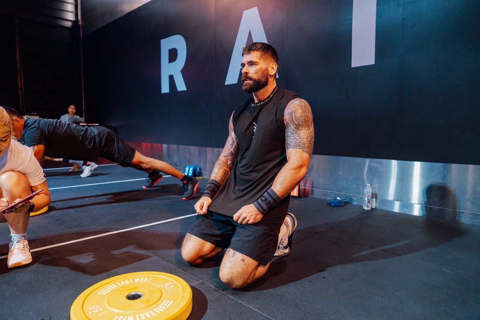 Steven kneeling beside a weight plate at a fitness competition